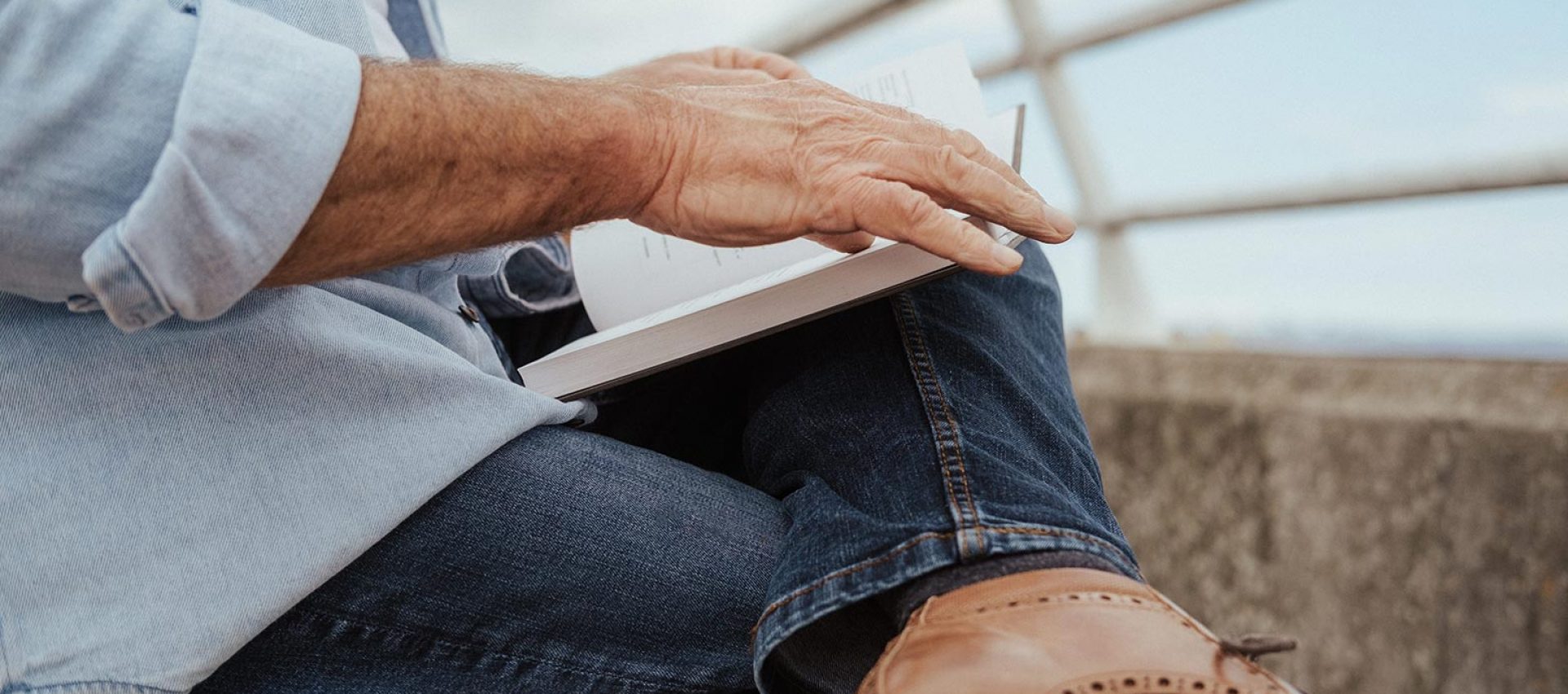 An older person is turning the page of a book that rests on their knee.